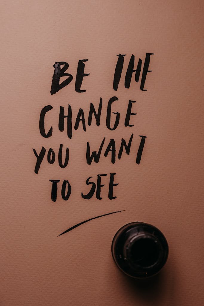 Inspirational message 'Be the change you want to see' in black ink on pink surface.